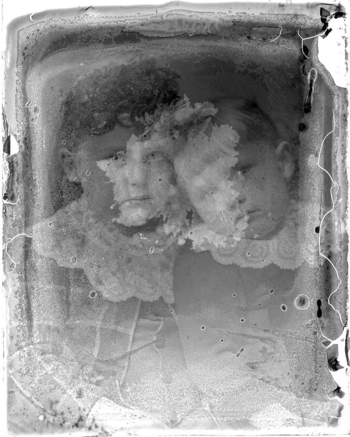 A scan of the damaged photographic plate. The damage is still evident, but the portrait of two children can be seen. It's difficult to make out most of their clothing, but one is earring a plaid outfit with buttons and they're both wearing lace collars.
